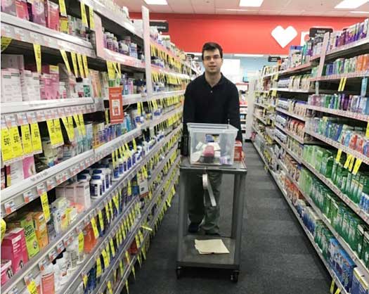 You man pushing a cart down the aisle at a CVS store stock the shelves