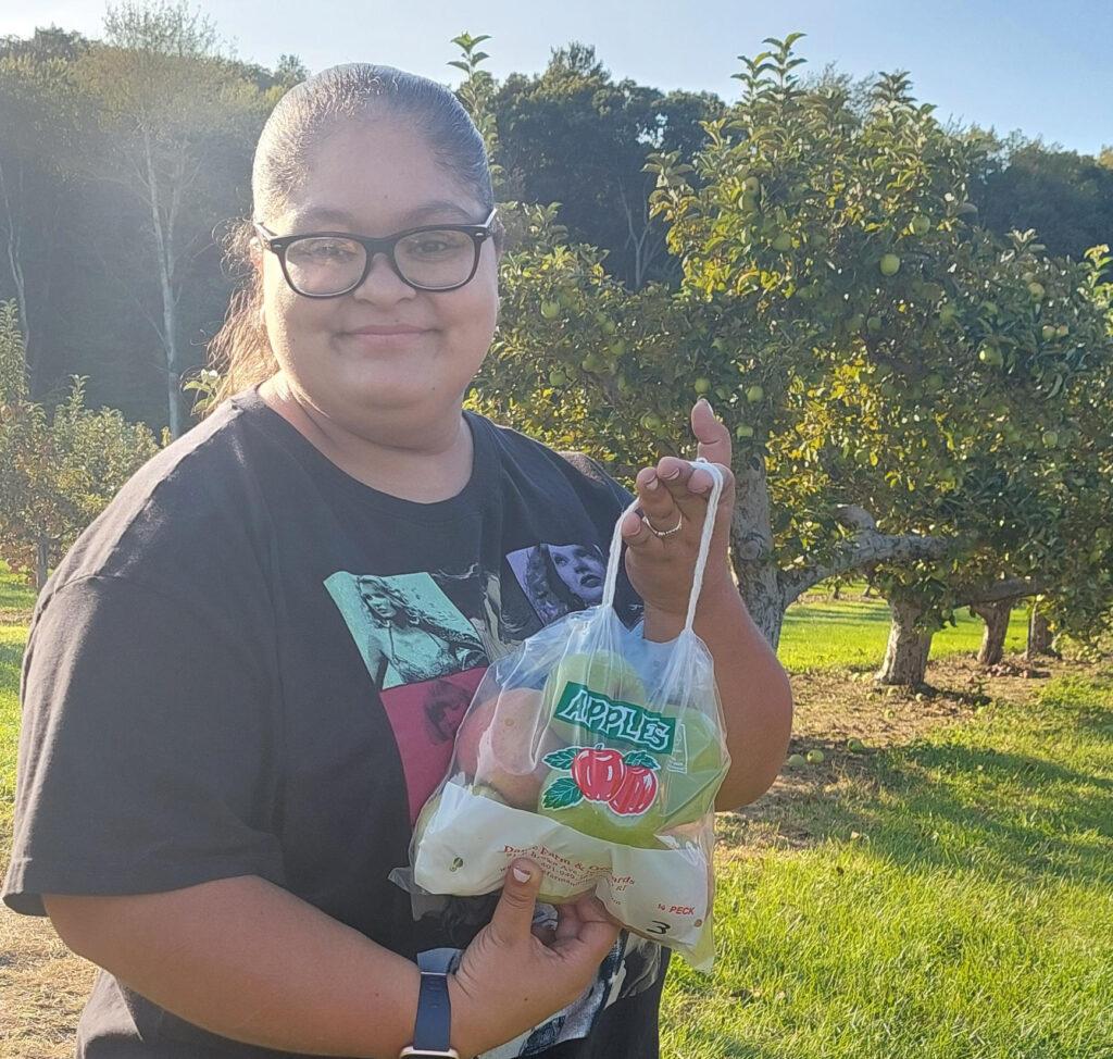 An AccessPoint RI patron poses at an apple orchard holding a bag of apples