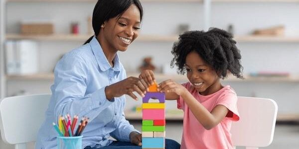 An African-American teacher works with a young African-American student to build a tower with toy blocks