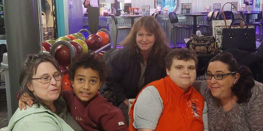 A group of smiling participants and caregivers hanging out at a bowling alley